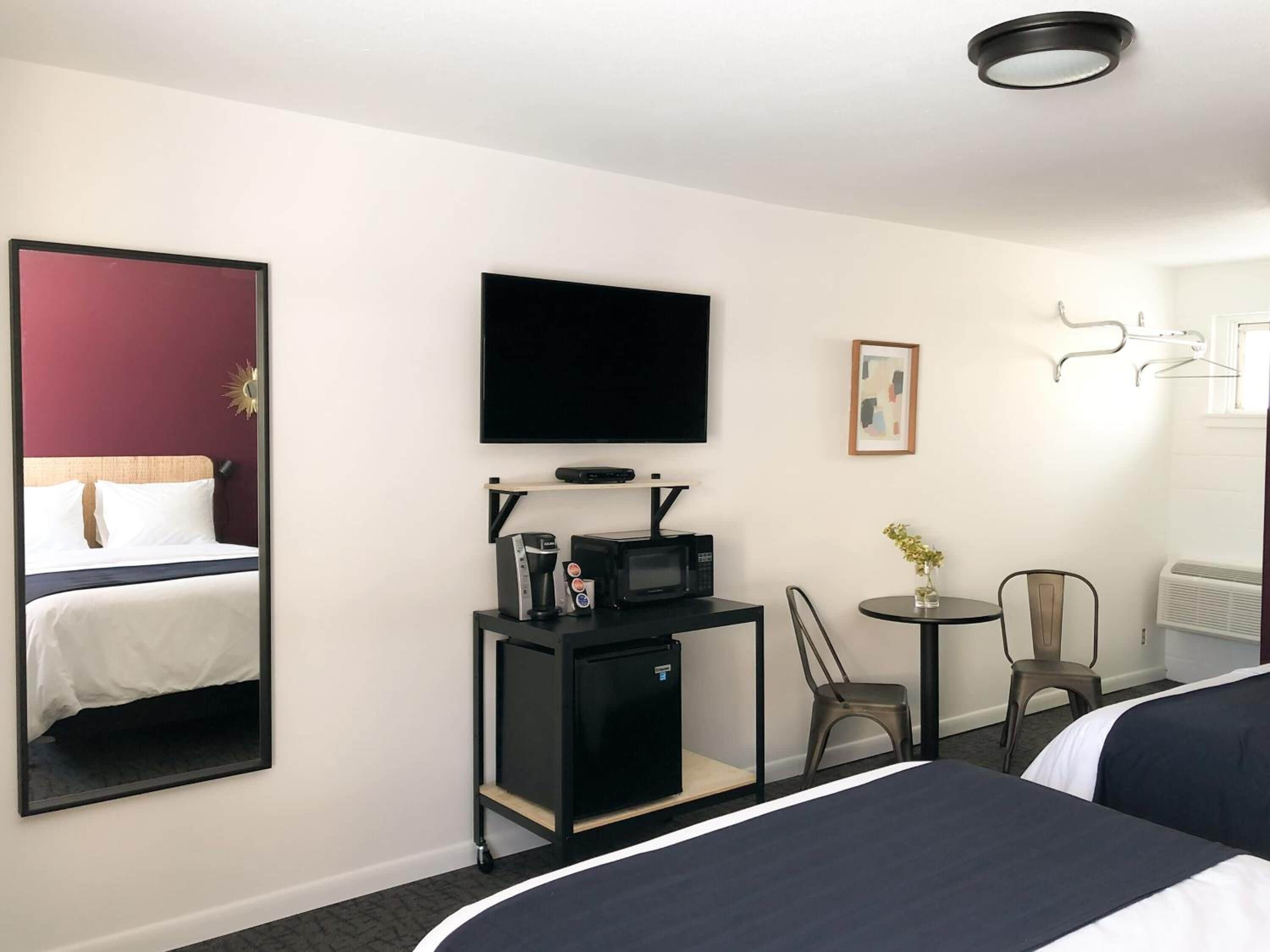 A hotel room with two beds, a desk with a coffee maker, a TV, and a mirror.