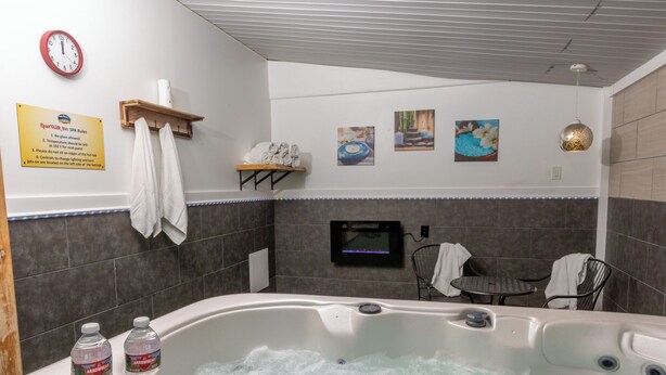 A spa room with a hot tub, a clock, a sign with spa rules, and artwork on the wall.