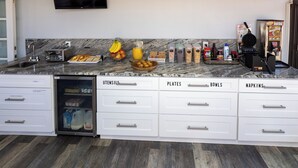 A kitchen with a built-in refrigerator, a microwave, and a waffle maker. There are various food items and condiments on the counter.