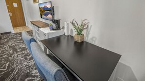 A hotel room with a dark wooden table, a white coffee machine, a woven plant pot, and a framed picture on the wall.