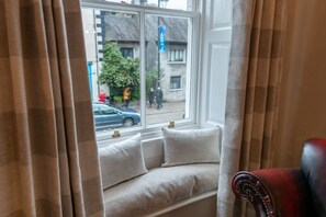 Un siège de fenêtre agrémenté de coussins, une vue sur la rue et un fauteuil rouge.