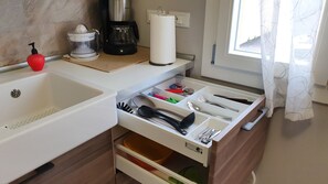 A kitchen with a sink, a coffee maker, a juicer, and a drawer organizer with utensils.