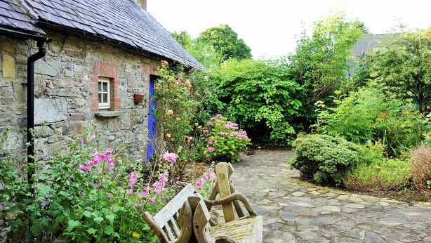A stone cottage with a thatched roof, a narrow stone pathway, and lush greenery. - Restored Historic Cottage in County Kilkenny (Carrickshock)