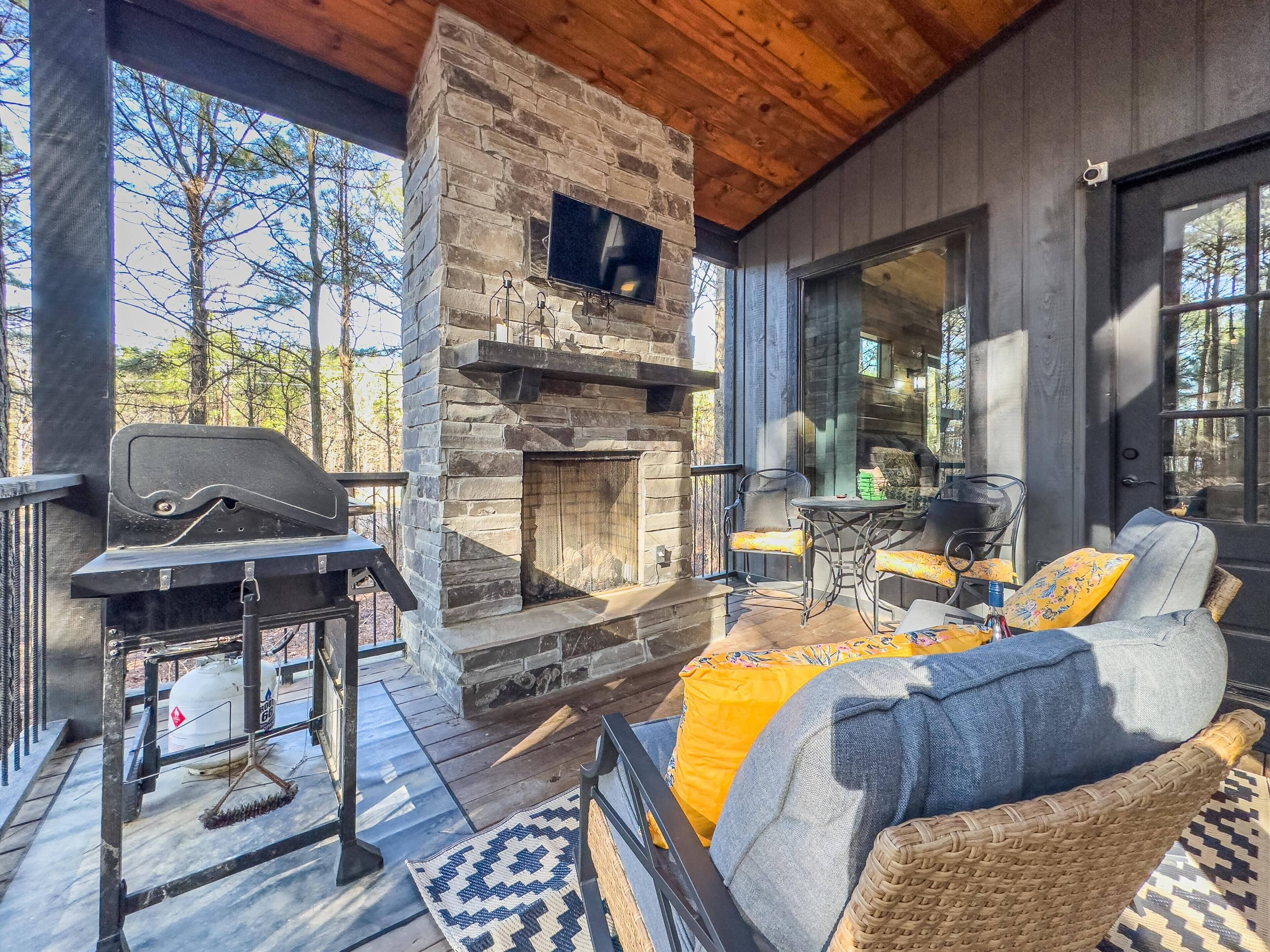 A cozy outdoor seating area with a stone fireplace, a grill, and wicker furniture.