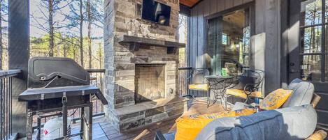 A cozy outdoor seating area with a stone fireplace, a grill, and wicker furniture.