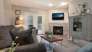 A living room with a fireplace, a television mounted on the wall, and a sofa set. - 2103 Golf View Towers Lazy Bears Den (Pigeon Forge)