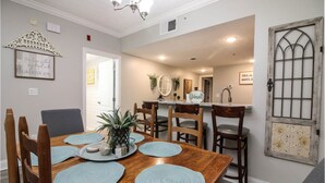 A dining area with a wooden table, six chairs, and a kitchen in the background. - 2103 Golf View Towers Lazy Bears Den (Pigeon Forge)