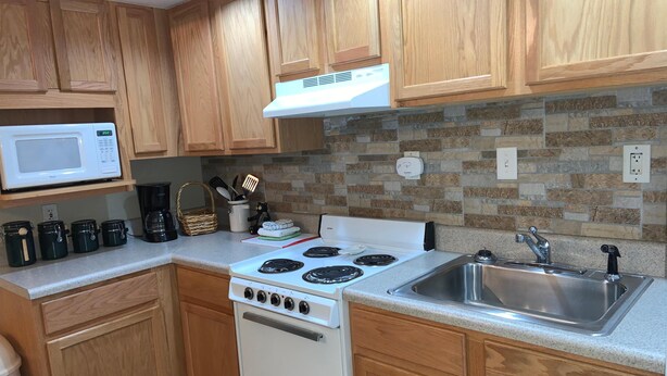 A compact kitchen with wooden cabinets, a white microwave, a stove, and a sink.