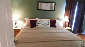 A neatly made bed with a pillow that reads "ALWAYS KISS ME goodnight" and a mirror on the wall.