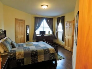 A bedroom with a bed, dresser, and a window with curtains.