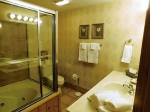A bathroom with a glass-enclosed shower, a toilet, a sink, and two framed pictures on the wall.