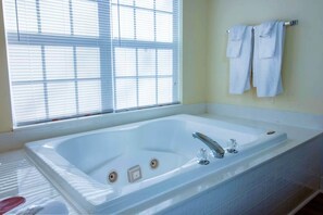 Ein modernes Badezimmer mit einer großen Badewanne, einem Fenster mit Jalousien und zwei weißen Handtüchern, die an einem Metallhandtuchhalter hängen.