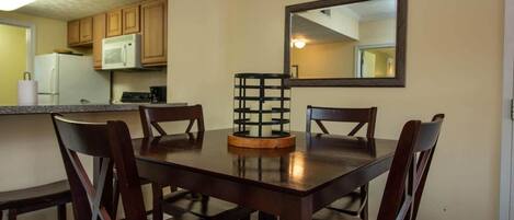 A dining area with a wooden table and four chairs, a candle holder, and a kitchen in the background.