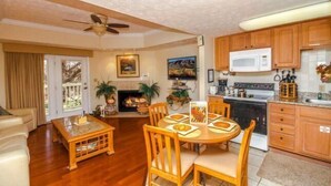 A living room with a fireplace, wooden dining table, and chairs. There is a kitchen with wooden cabinets and a microwave. - 1501 Golf View Towers Southern Comfort (Pigeon Forge)