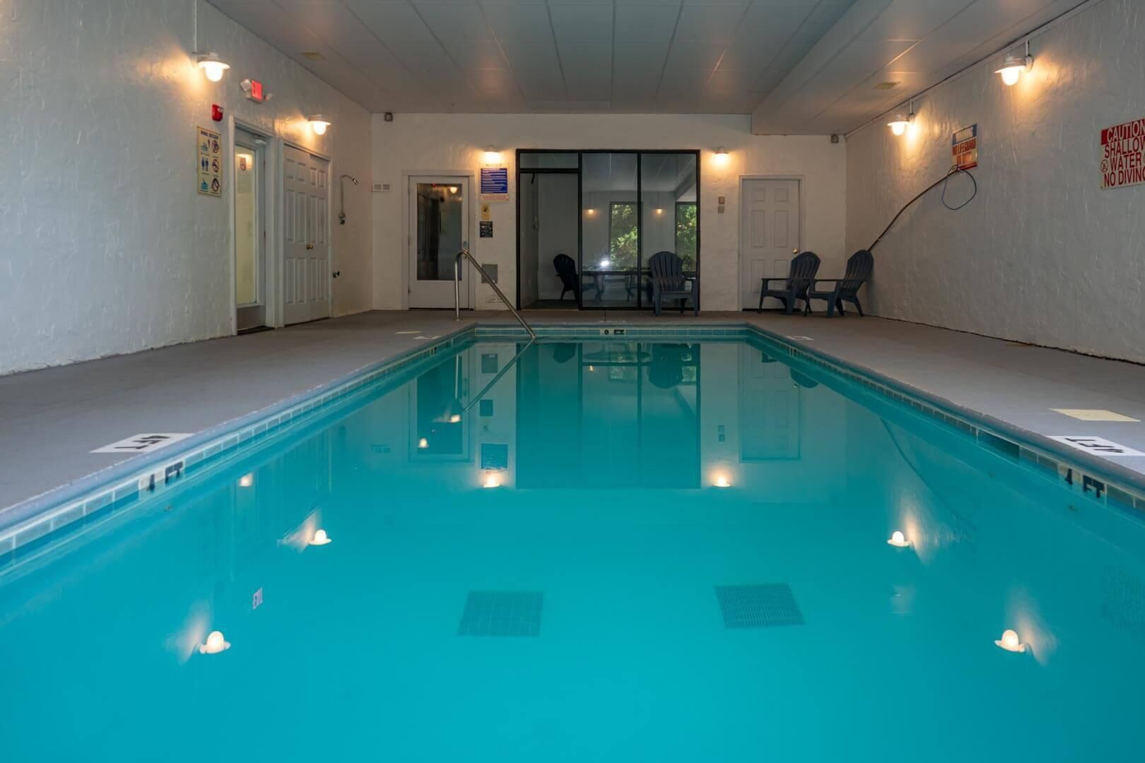 An indoor swimming pool with clear water, surrounded by walls with light fixtures and safety signs.