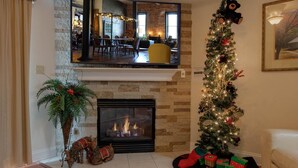 A cozy living room with a fireplace, a Christmas tree, and a dining area visible through a glass partition. - 1501 Golf View Towers Southern Comfort (Pigeon Forge)