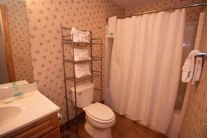A bathroom with a toilet, a shelf with towels, and a shower curtain.