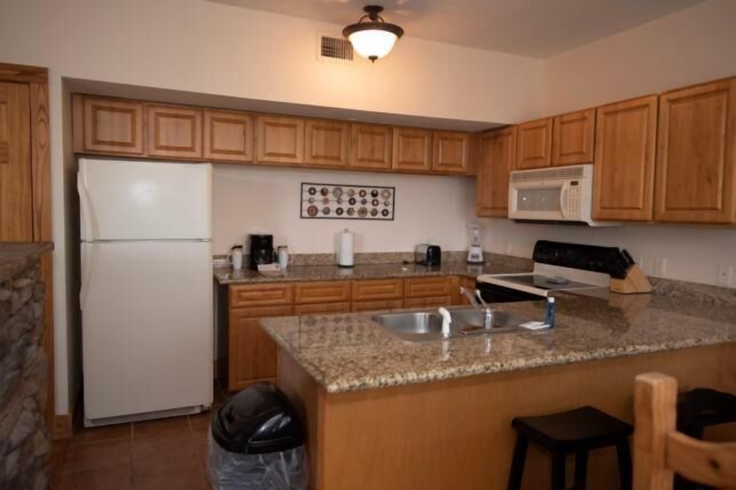 A kitchen with wooden cabinets, a granite countertop, a refrigerator, a microwave, and a sink.