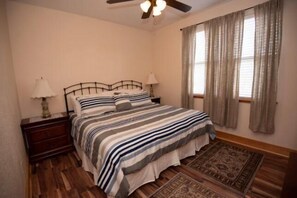 A bedroom with a bed, nightstands, lamps, a ceiling fan, and a window with curtains.