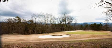 A golf course with a sand bunker, trees, and a cloudy sky.