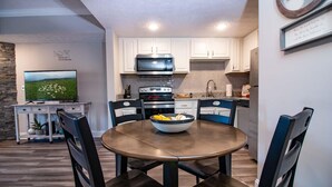 A modern kitchen with white cabinets, a microwave, stove, and a dining area with a round table and chairs. - 2501 Golf View Towers Almost Home (Pigeon Forge)
