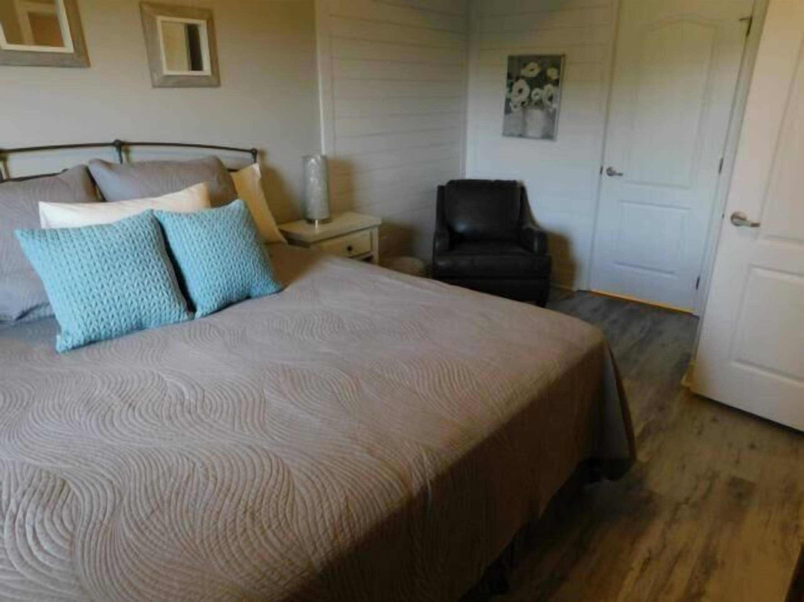 Une chambre à coucher avec un lit, des oreillers, une chaise, une table de chevet et une porte.