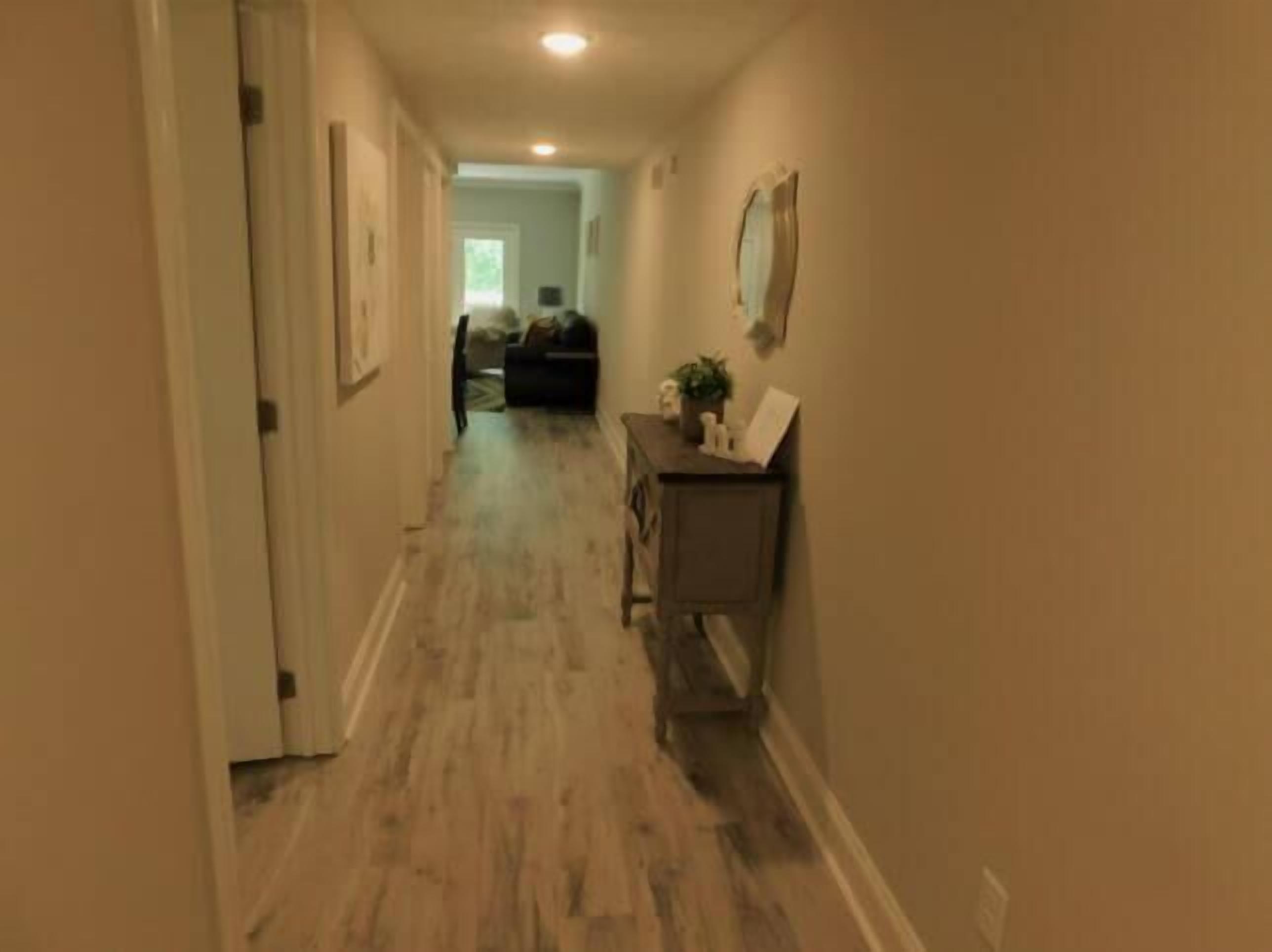 A hallway with wooden flooring and beige walls, leading to a living area with a couch and a coffee table.