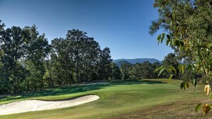 A golf course with a sand bunker, trees, and a clear sky. - 1404 Golf View Towers Smoky Mtn Bearadise (Pigeon Forge)