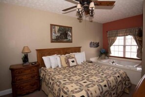 A bedroom with a bed, a nightstand, a dresser, a window with curtains, a ceiling fan, and a painting on the wall.