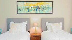 Une chambre d’hôtel avec deux lits, une table de chevet avec une lampe et un tableau abstrait aux couleurs vives accroché au mur.
