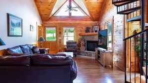 A cozy cabin interior with a wooden ceiling, a fireplace, a leather sofa, and a television. - 839a Golf View Cabins Rockin' Robin (Pigeon Forge)