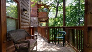 A wooden deck with wicker chairs and a green plastic chair, overlooking a forested area. - 839a Golf View Cabins Rockin' Robin (Pigeon Forge)