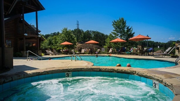 A pool area with a hot tub, lounge chairs, and umbrellas. - 839a Golf View Cabins Rockin' Robin (Pigeon Forge)
