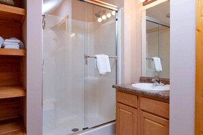 A modern bathroom with a glass-enclosed shower, a wooden vanity with a sink, and a mirror above the vanity.
