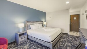 A hotel room with a bed, bedside lamps, a wooden headboard, a nightstand, a chair, and a door. - Downtown King room w/ San Juan River & Mtn Views (Pagosa Springs)