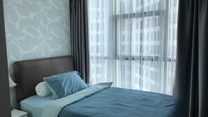 A modern hotel room with a neatly made bed, a nightstand, and a window with sheer curtains.