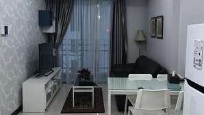 A modern living room with a sofa, a TV, a dining table with chairs, and a small coffee table.