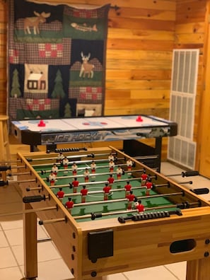 A foosball table in a room with wooden walls and a blanket with animal prints.