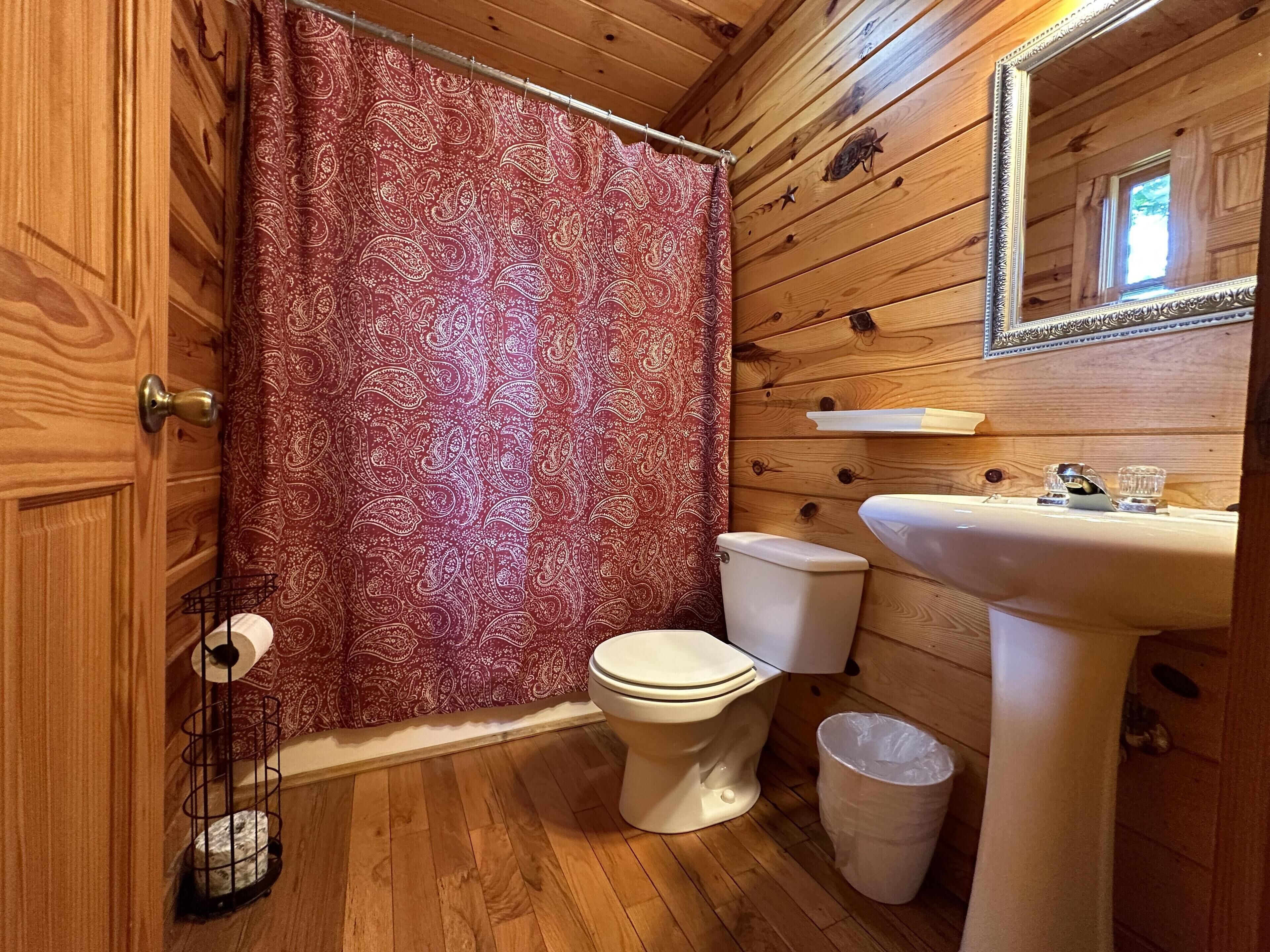 A wooden cabin bathroom with a toilet, sink, and shower curtain.