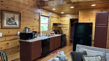 A wooden cabin interior with a kitchen area, a dining table, and a couch.