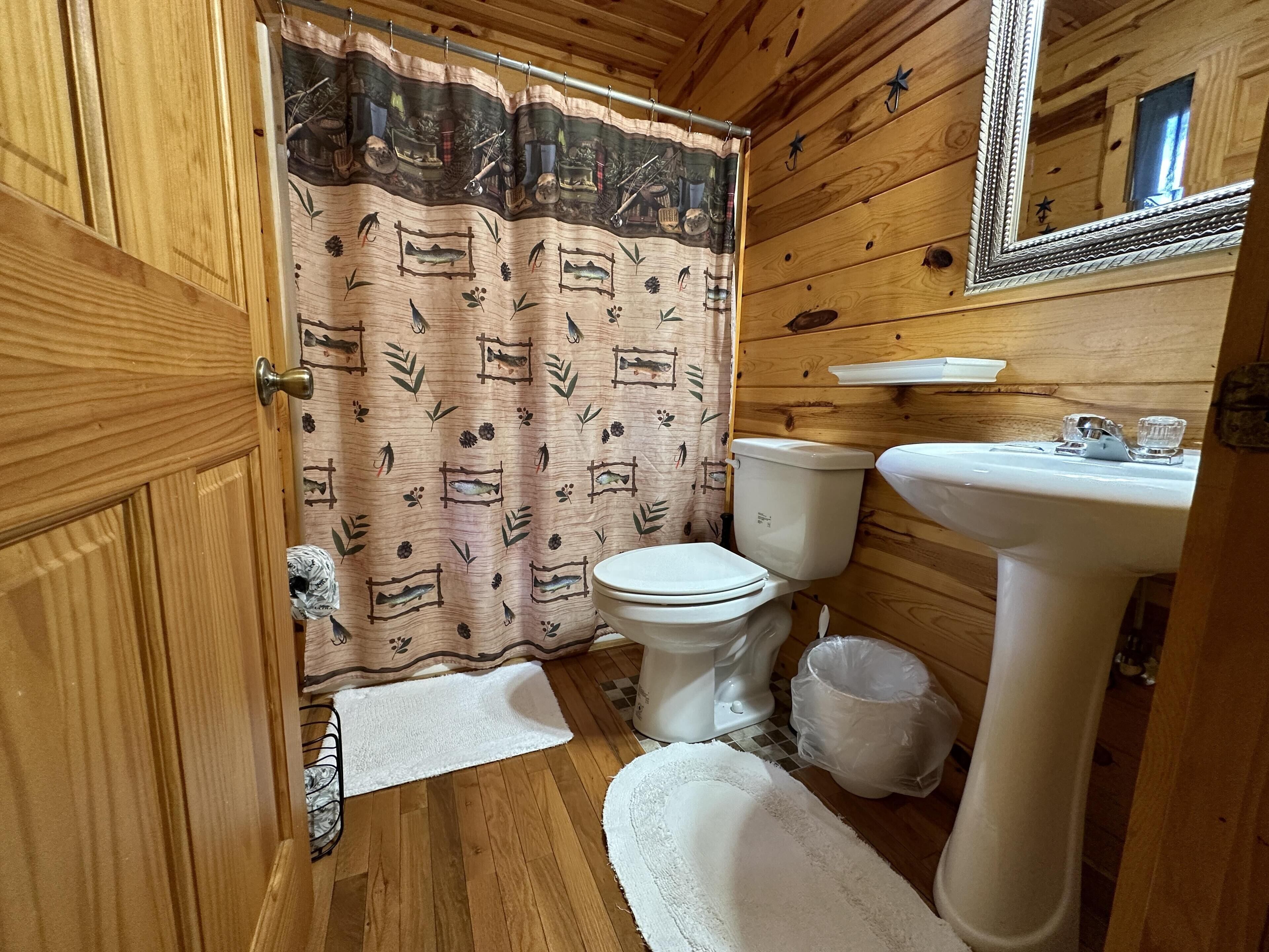 Baño de cabaña de madera con inodoro, lavabo y cortina de ducha.