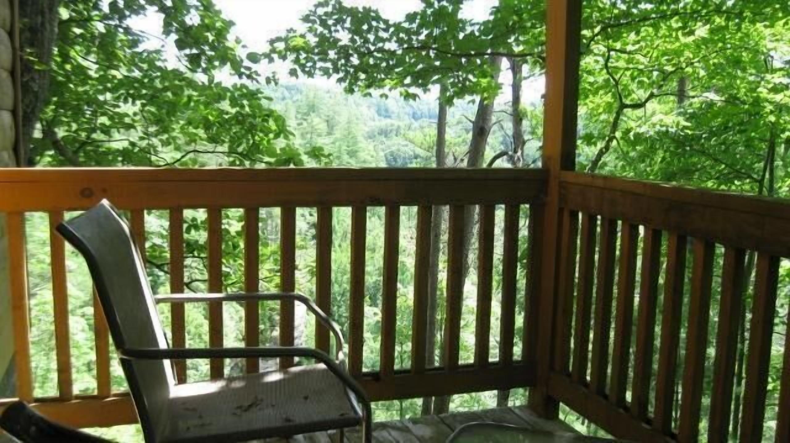 A wooden deck with a metal chair, overlooking a forested area.