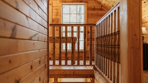 Un escalier en bois avec une rampe, menant à une fenêtre d’où l’on peut admirer les arbres.