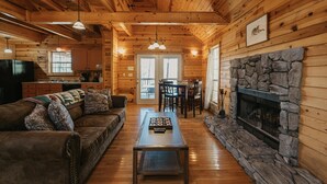 L’intérieur d’un chalet accueillant, avec une cheminée en pierre, des murs en bois, un coin repas et un salon comprenant un canapé et une table basse.