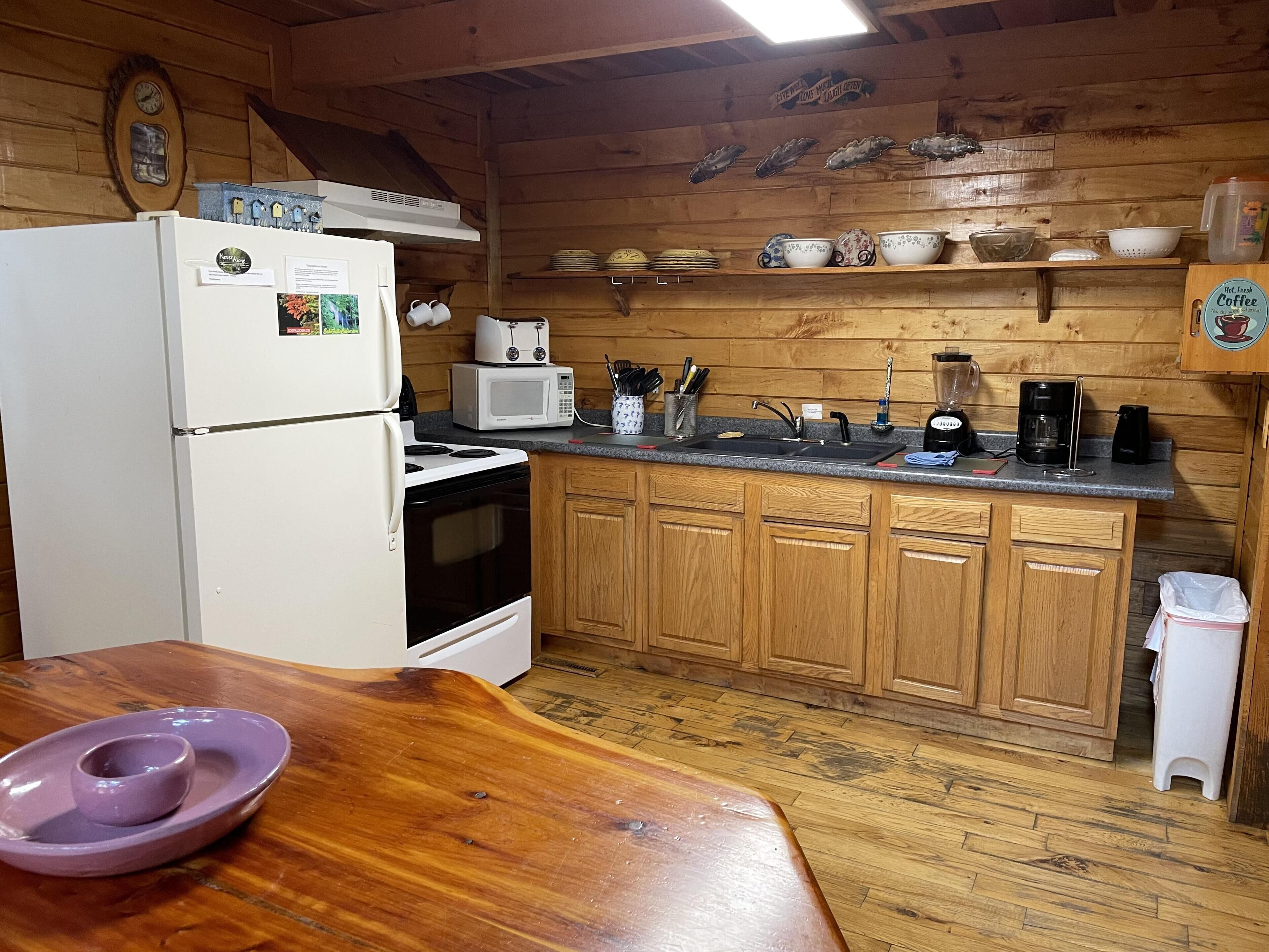 A compact kitchen with wooden cabinets, a refrigerator, a microwave, a stove, and a coffee maker.