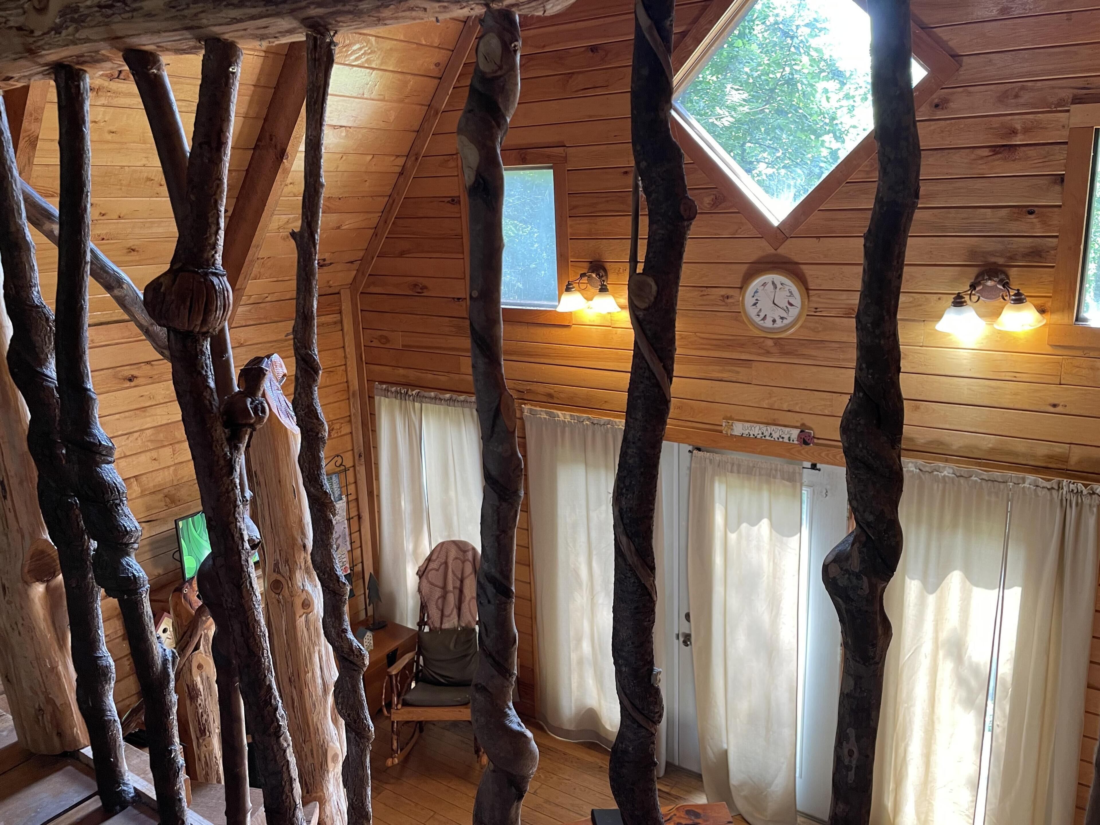 Une pièce rustique avec des murs en bois et des poutres apparentes, un plafond en bois et une lucarne. Il y a une horloge au mur et une chaise dans un coin.