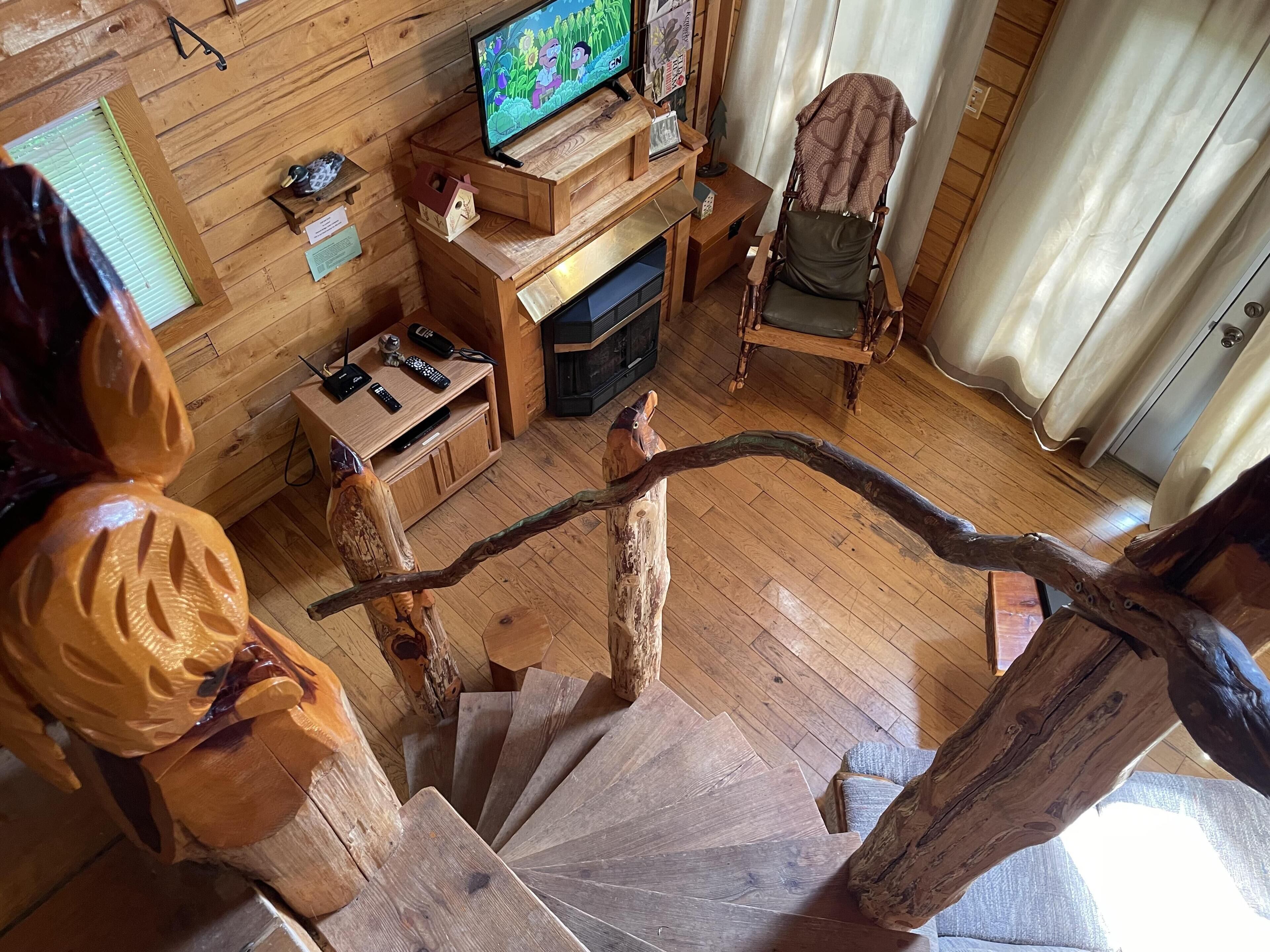 Un interior de madera con una televisión sobre un mueble de madera, una silla y una escalera con barandilla de madera.