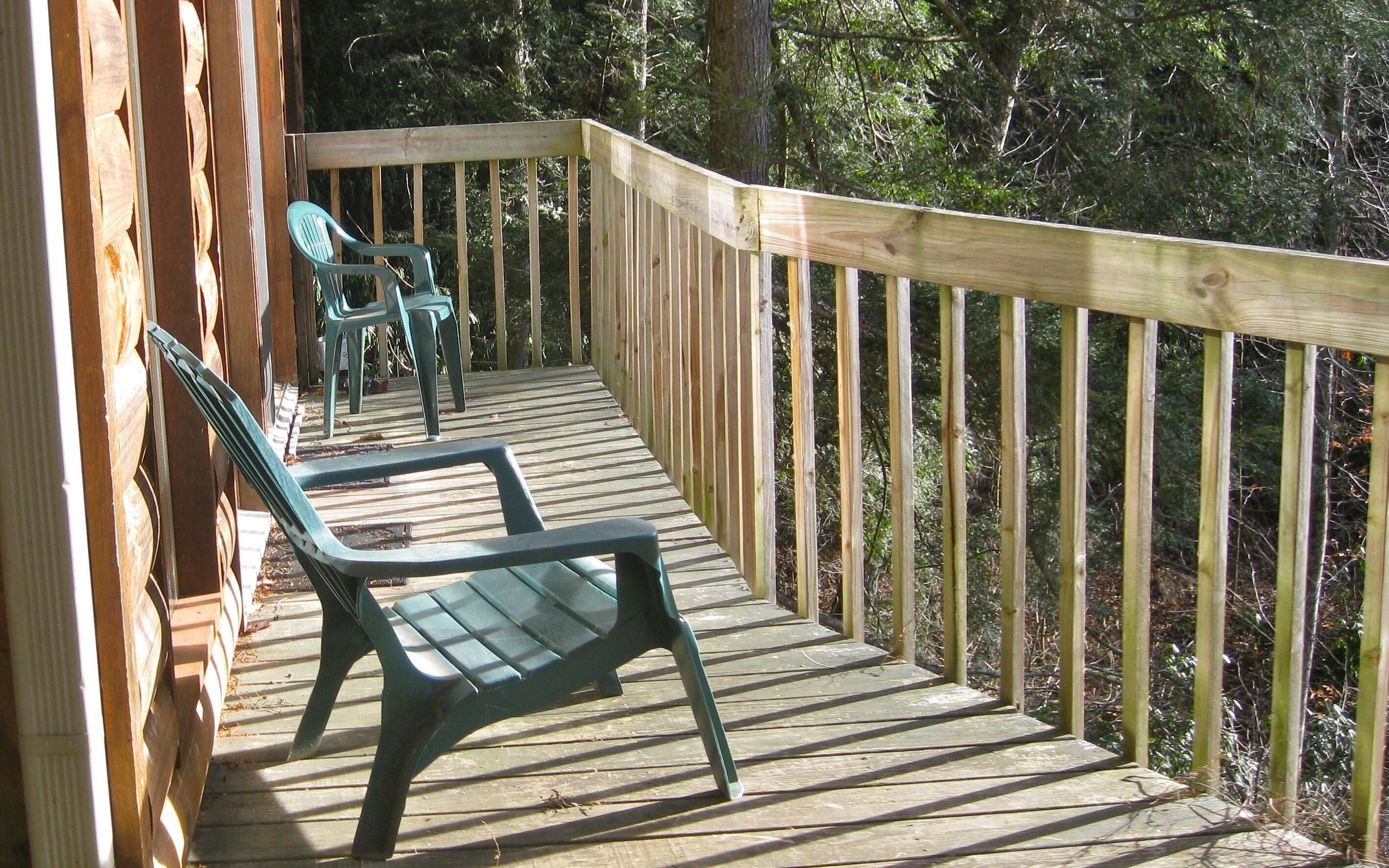 Une terrasse en bois avec deux chaises en plastique vertes et une table, le tout entouré d’une balustrade en bois.