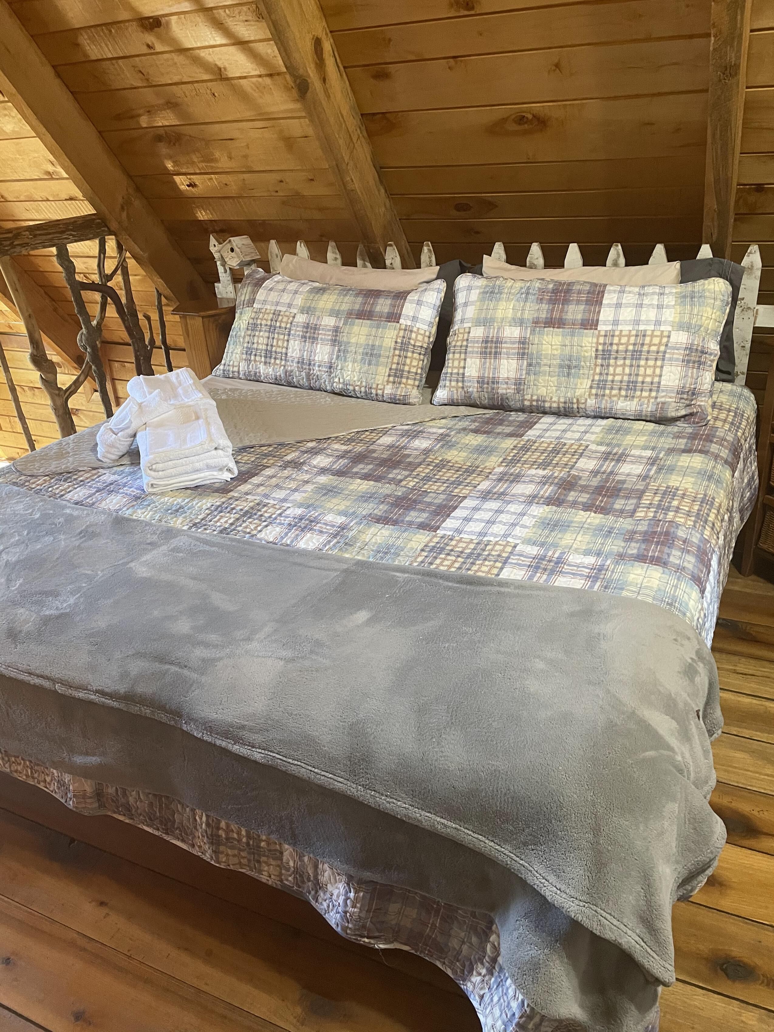 Una cama de madera con ropa de cama escocesa y una manta gris en una cabaña rústica.