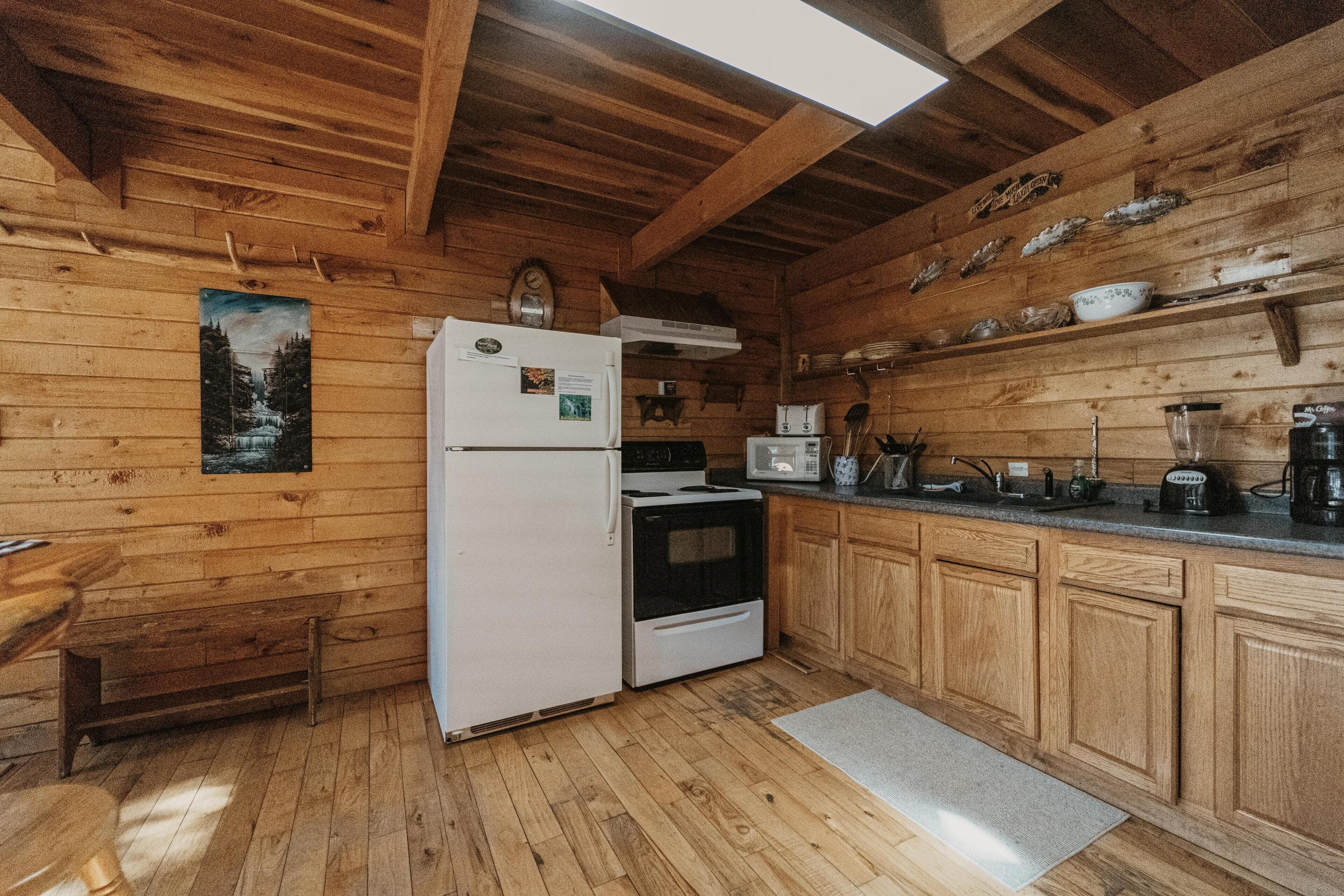 A wooden cabin kitchen with a refrigerator, stove, microwave, and wooden cabinets.
